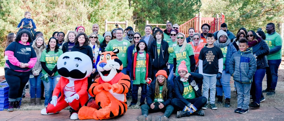 Group photo of volunteers with mascots Tony the Tiger and Pringles, gathered at a community playground event.
