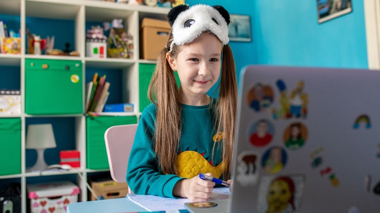 A student with a panda mask on her forehead looks at a laptop while completing schoolwork